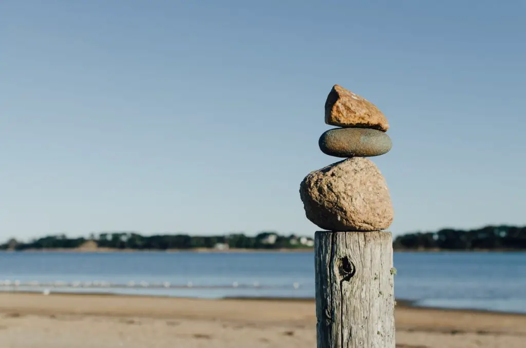 rock balancing on wooden post near body of water flow qi