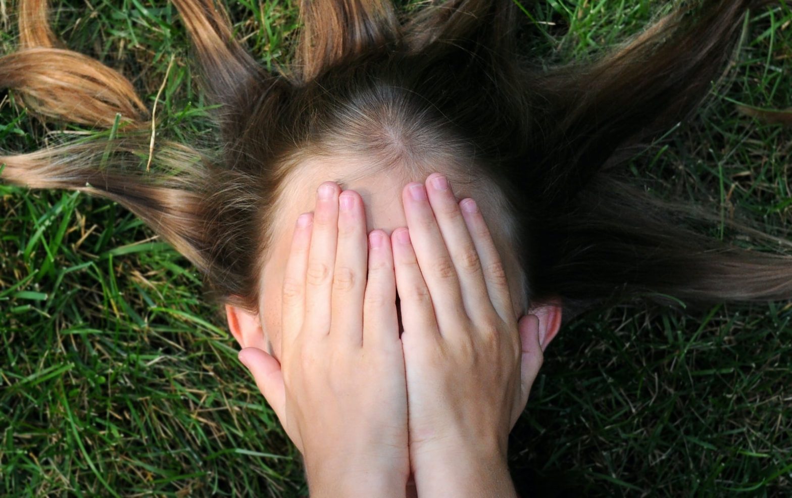 woman covering her face with acne lying on green grass