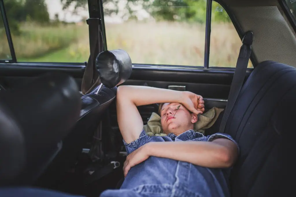 person in blue denim shirt sleeping behind the car seat drunk