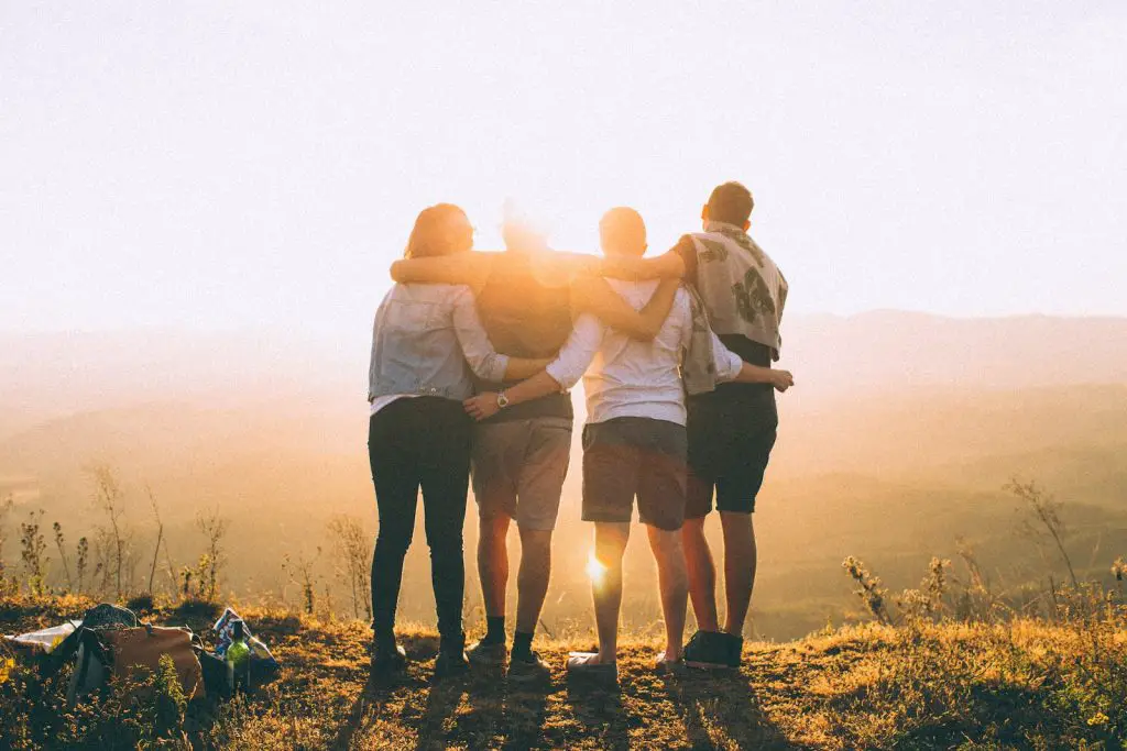 30 Second Hug Benefits: All the Health Benefits 2 four person hands wrap around shoulders while looking at sunset
