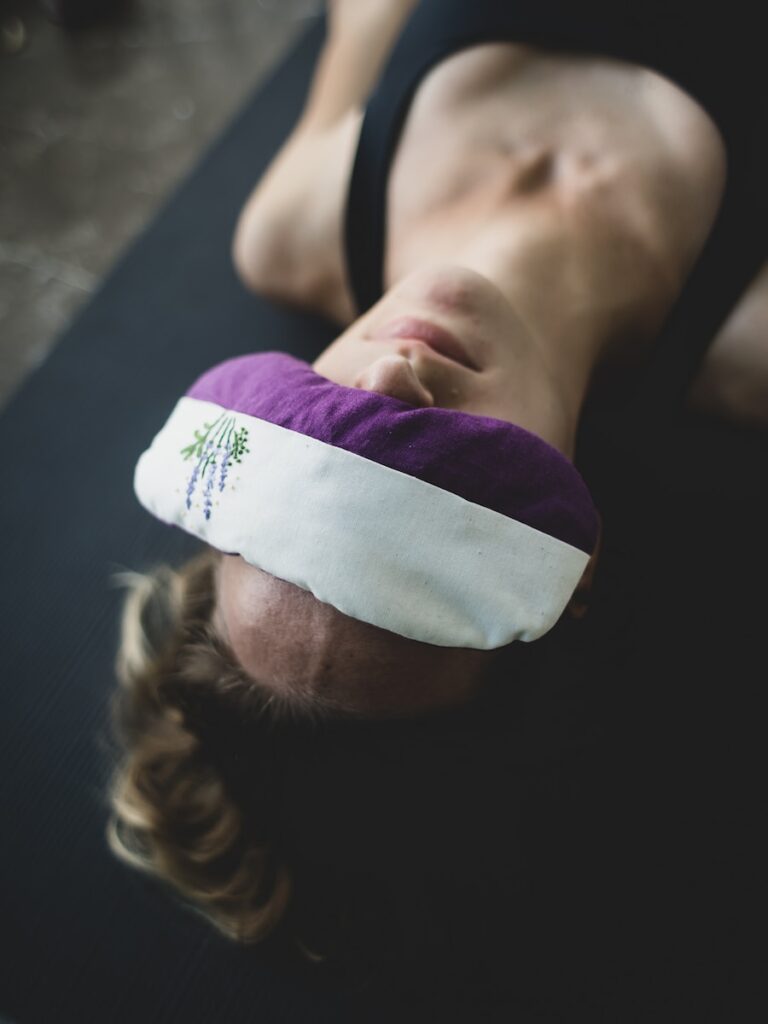 woman put purple and white pad on her forehead savasana yoga nidra