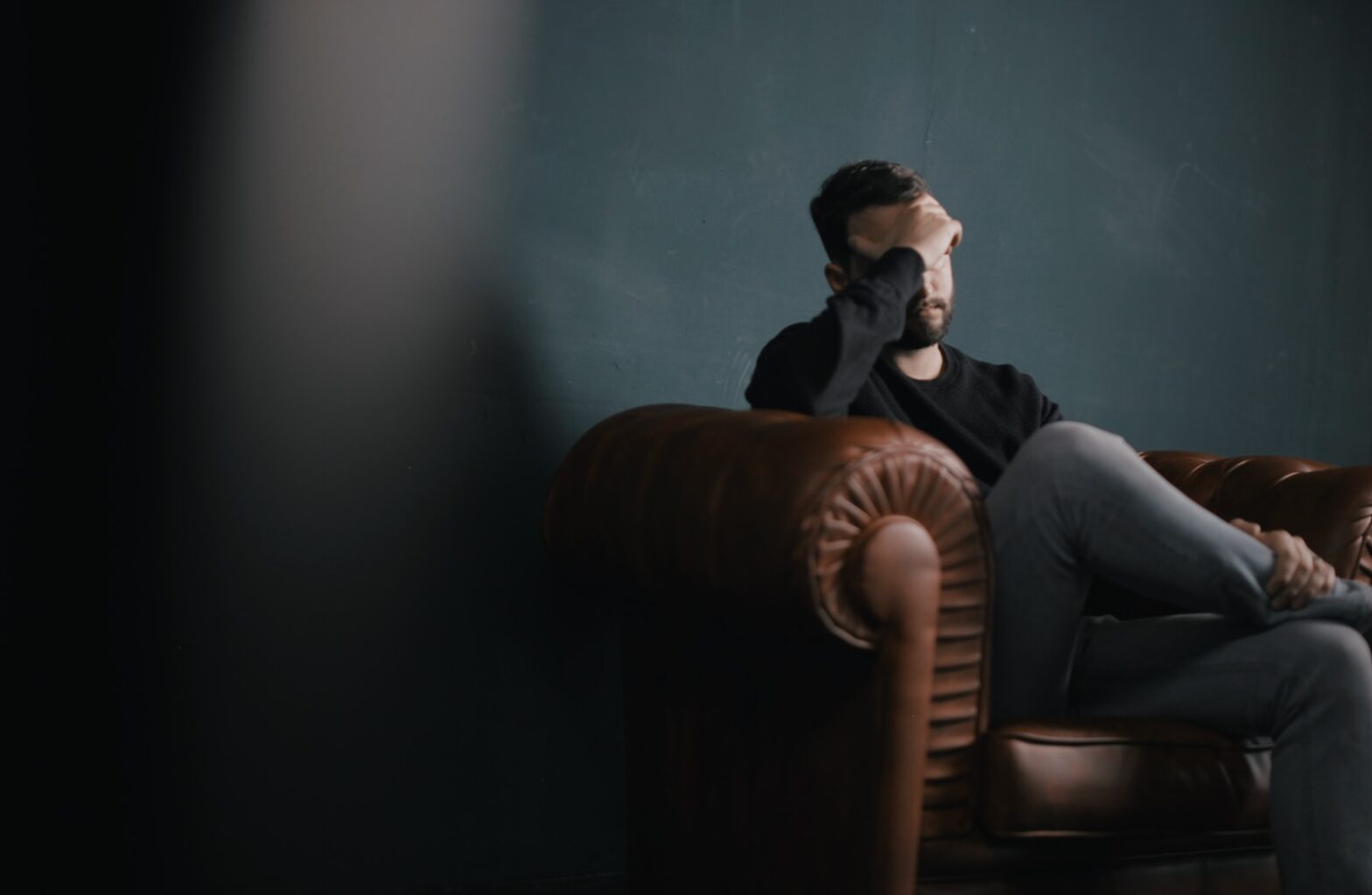 a man holds his head while sitting on a sofa. mental health and sleep